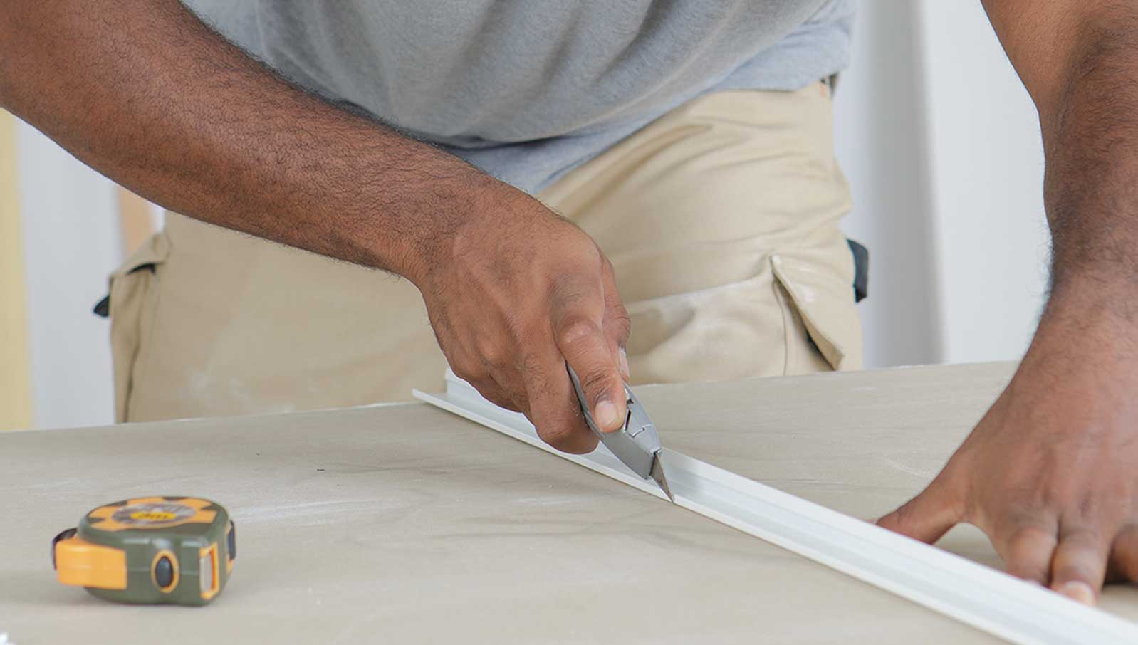 Eine Person schneidet ein Material mit einem Cuttermesser, neben einem Maßband auf einem Tisch