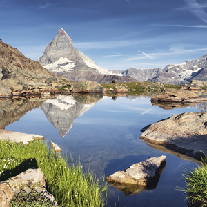 Das Matterhorn spiegelt sich in einem klaren Bergsee, umgeben von einer alpinen Landschaft und klarem Himmel.